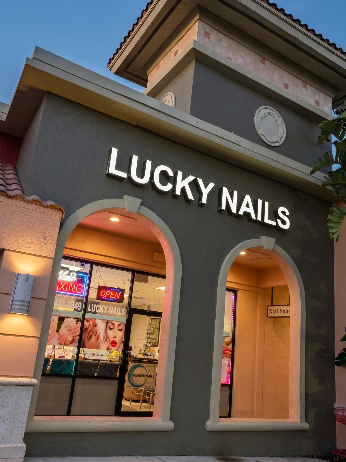 The lit Lucky Nails storefront sign above the arched entryway at dusk