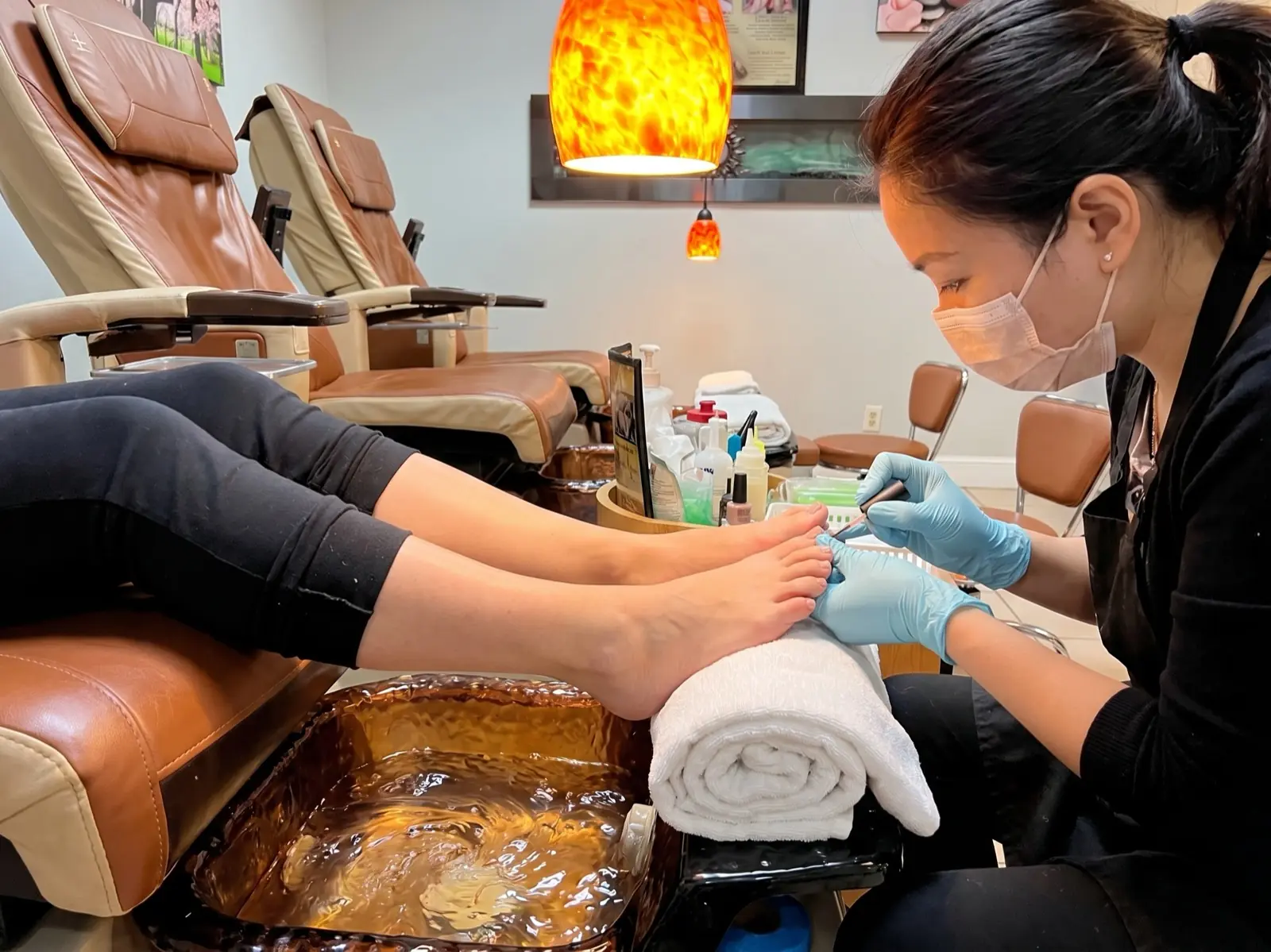 Technician applying toenail polish at a leather pedicure chair