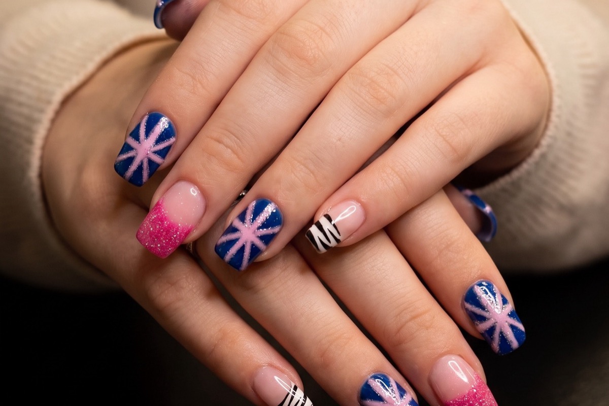 Navy nails with pink starburst art, pink glitter French tips and a black and white striped accent nail